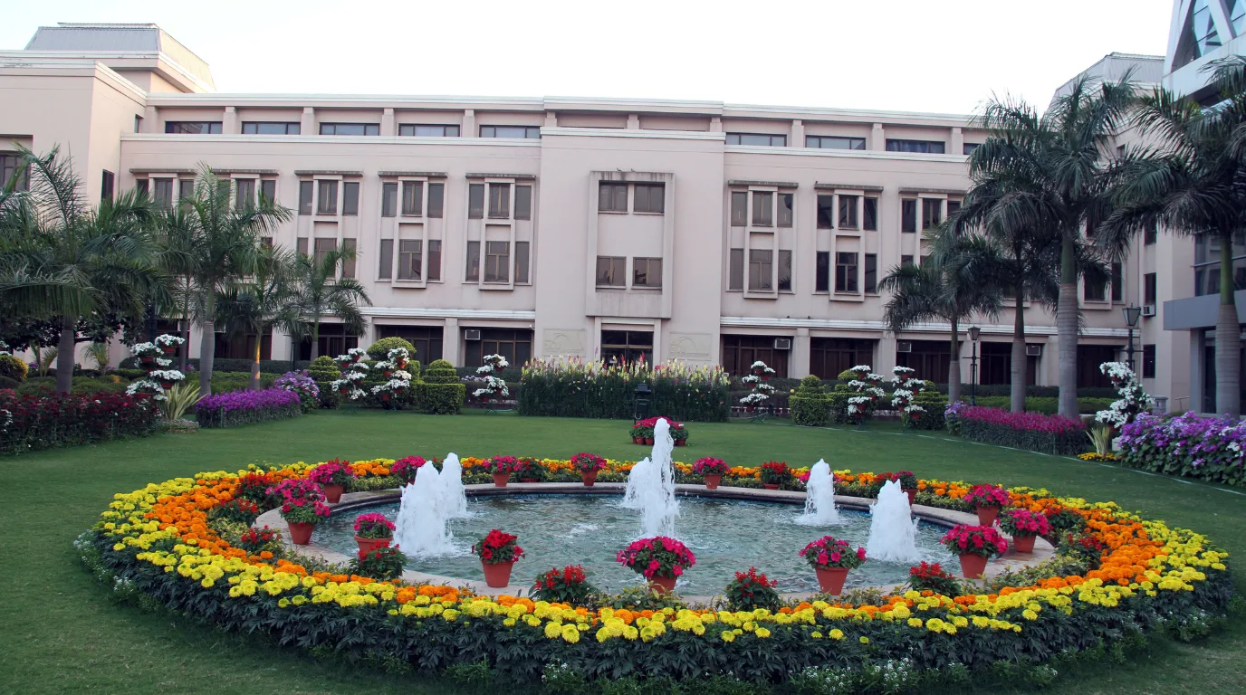 Fountain surrounded by marigold flower beds in front of The NorthCap University classic academic building